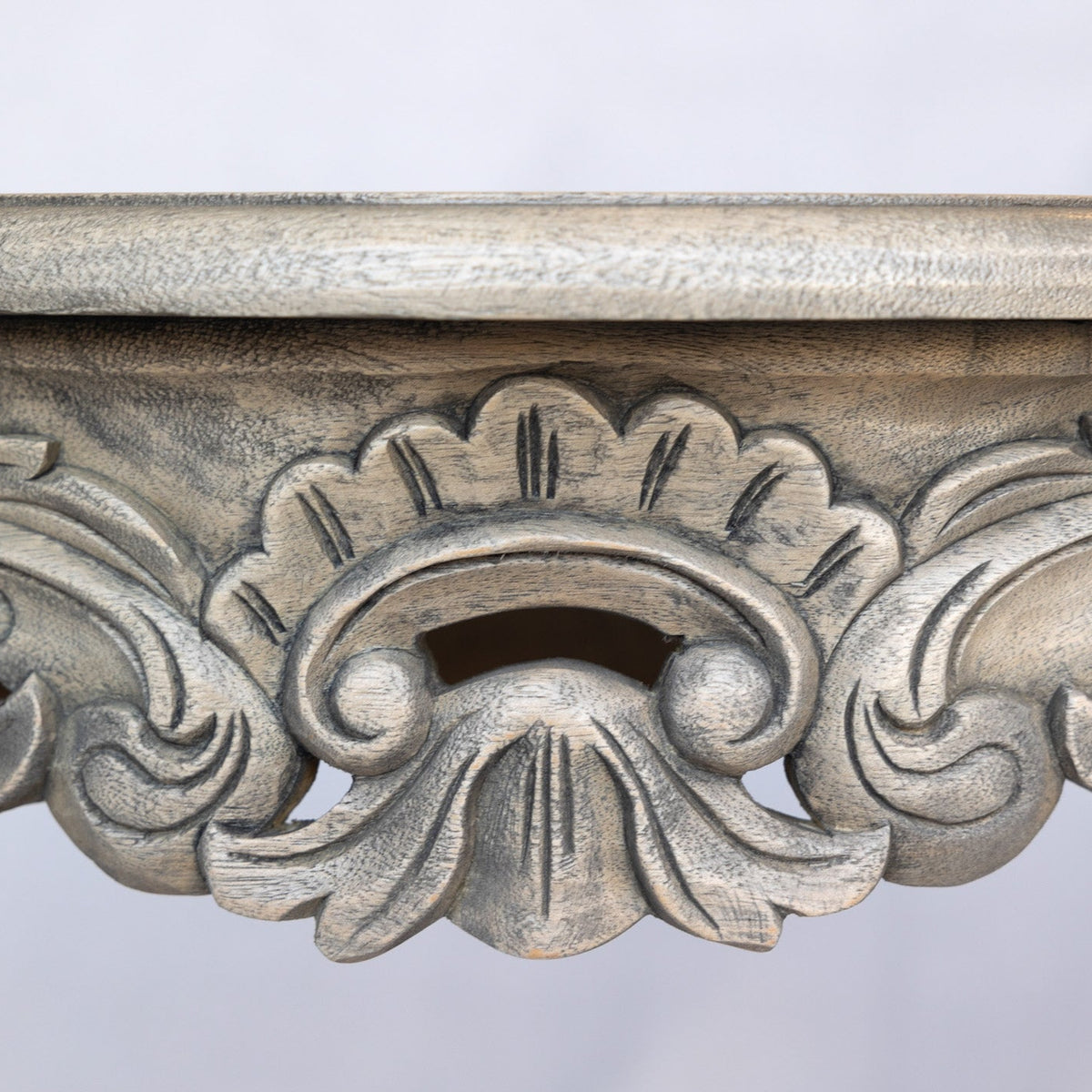 Close-up of an ornate carved console table apron with a distressed silver-gray finish and classical acanthus leaf details.