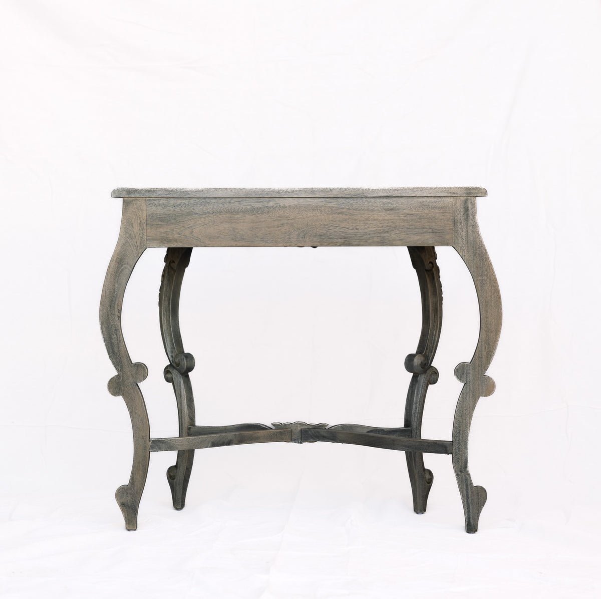 A distressed gray wooden console table with curved legs and a central stretcher bar, photographed against a white fabric backdrop.