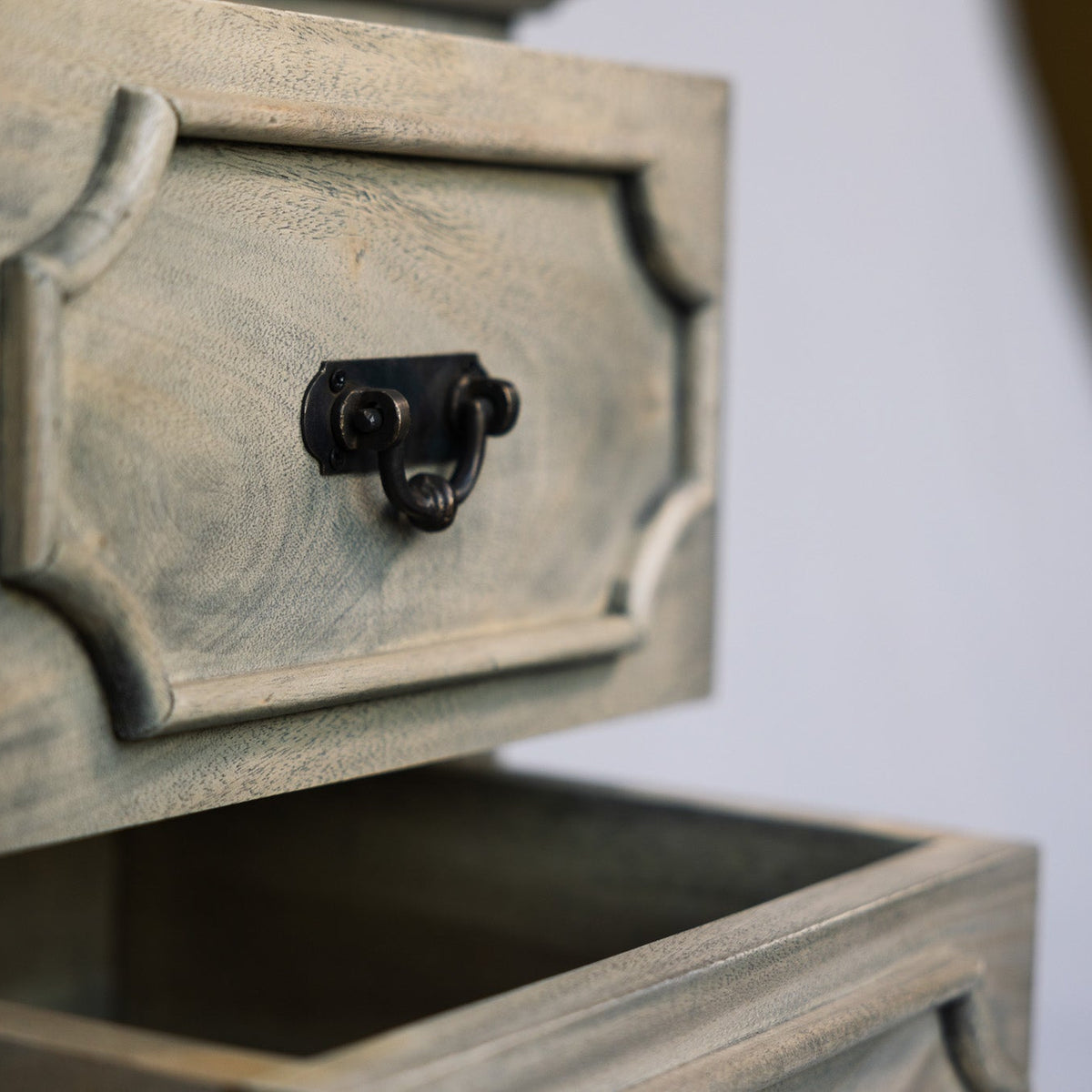 Close-up of a distressed gray wooden drawer with a black metal ring pull handle, shown against a softly blurred background.