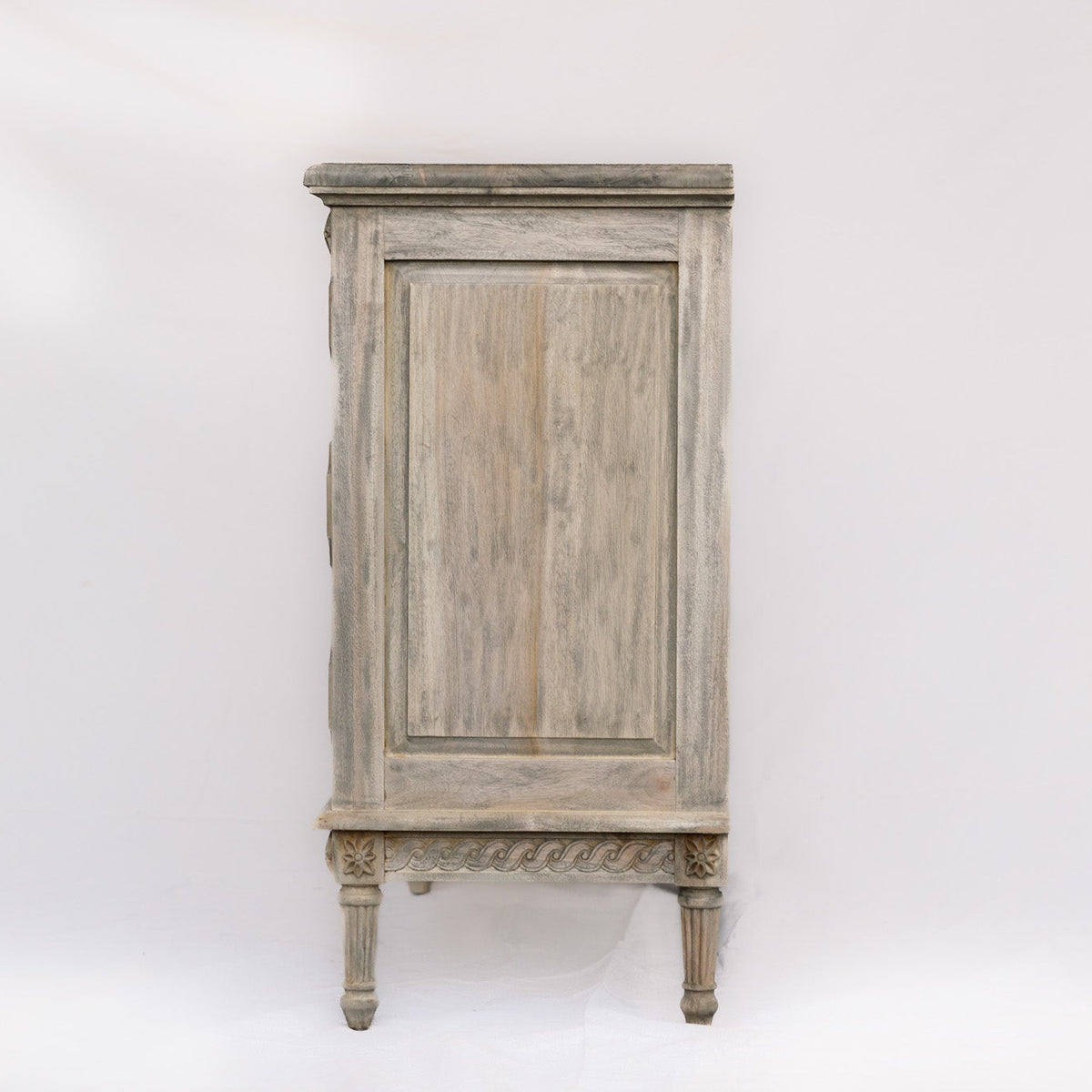 A distressed gray wooden cabinet with a single paneled door, ornate carved base, and four legs, photographed against a white studio background.