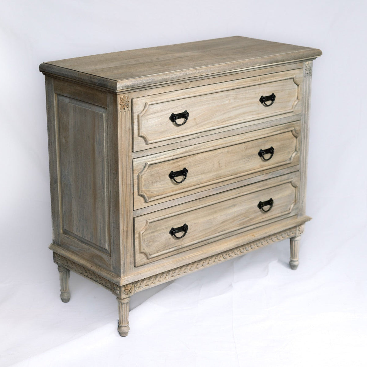 A three-drawer wooden chest of drawers with a distressed gray and beige finish, featuring dark metal handles and turned legs, photographed against a white studio backdrop.